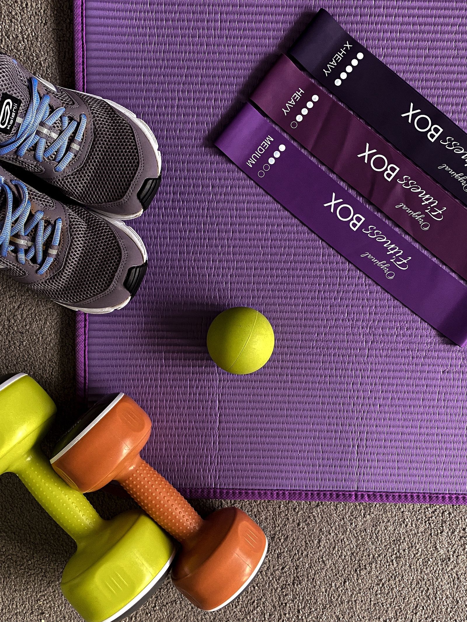 Lopta, utezi i sportska obuća uz prostirku